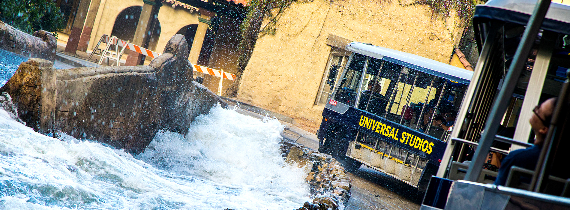 Universal Studios tram driving alongside crashing waves of water.